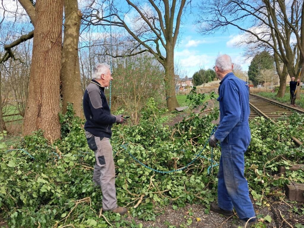 Tonnie en Piet staan tussen snoeiafval, naast het spoor.